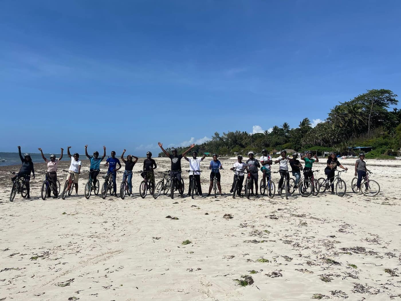 A long line of riders and bikes on the beach under a blue sky