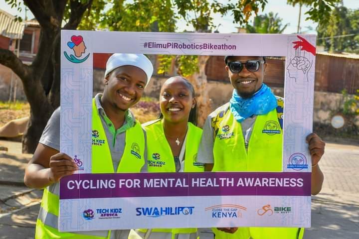 Riders holding a 'Cycling for mental health awareness' board with partner logos